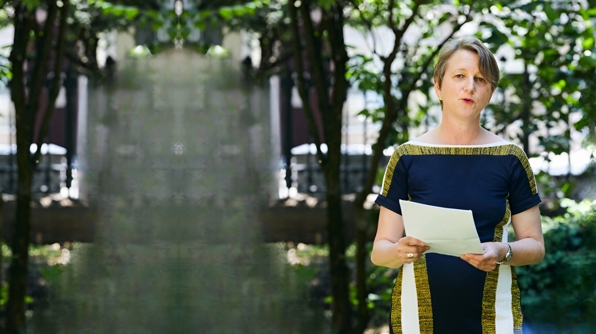 Anja Klug speaking at an event in a garden courtyard, addressing the audience with notes in hand.